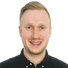 Junger Mann mit kurzen blonden Haaren, schwarzes Hemd, lächelndes Gesicht, sichtbare Schultern.