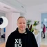 Ein Mann mit kurzem Bart trägt einen schwarzen Hoodie mit weißer Schrift 'XERO GRA' auf der Brust und lächelt.