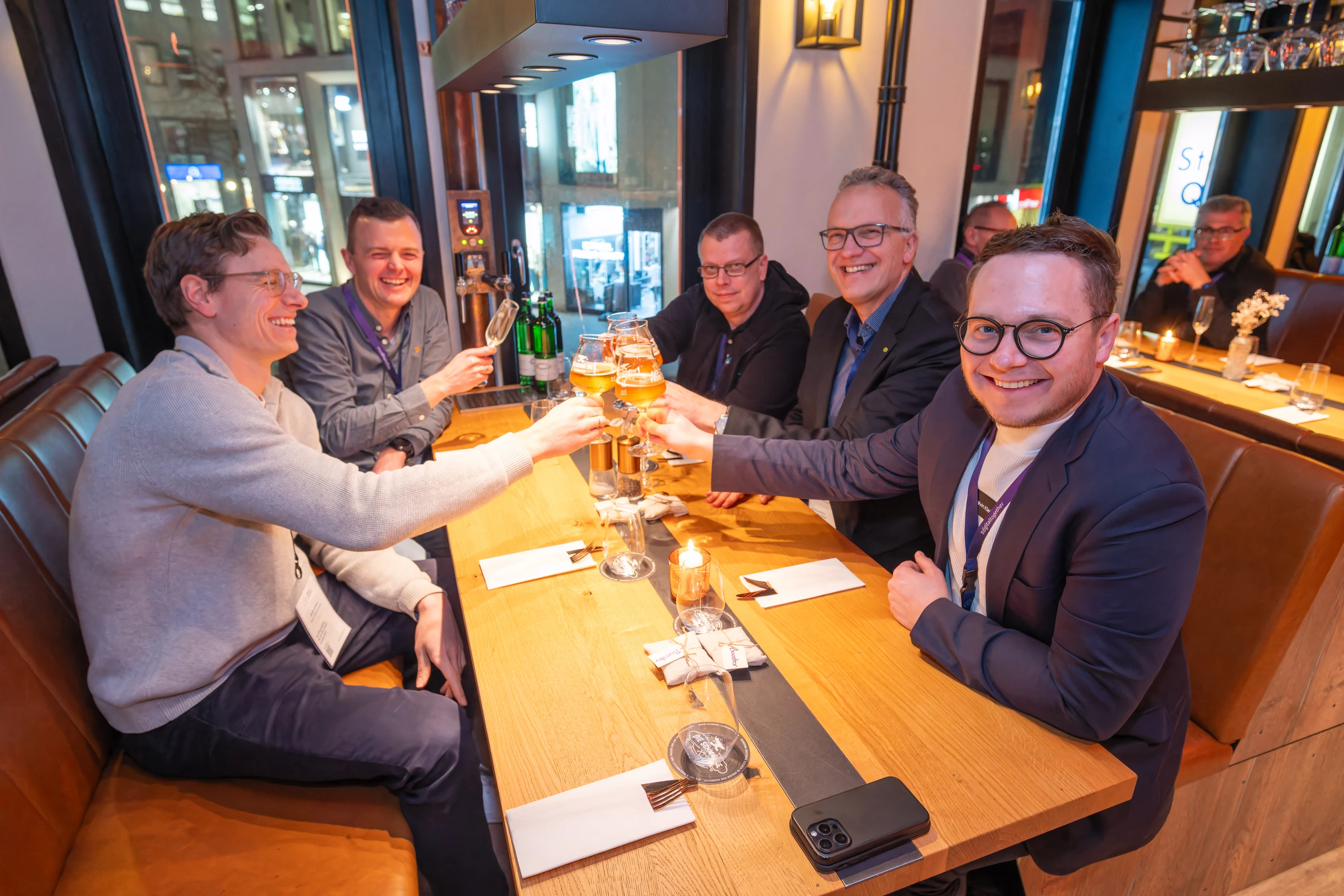 Mehrere Personen sitzen an einem Holztisch in einem Restaurant und stoßen mit Weingläsern an.