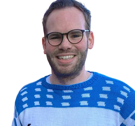 Mann mit Brille und Bart, blau-weißes Strickpullover, lächelt vor weißem Hintergrund.