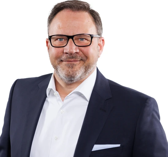 Mann mittleren Alters mit Brille, dunkelblauem Anzug, weißem Hemd und hellblauem Einsteck-Tuch, vor weißem Hintergrund.